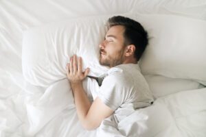 Sleeping man in white bed top view. Relaxed young bearded adult in cozy white bedroom having rest