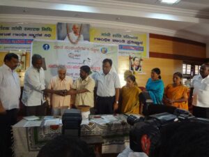 Devanura at the release of 'Edege Bidda Akshara'. Handing him a copy of the book is the famous poet, Dr Siddalingaiah. To Dr Siddalingaiah's left is Dr Nataraj Huliyar