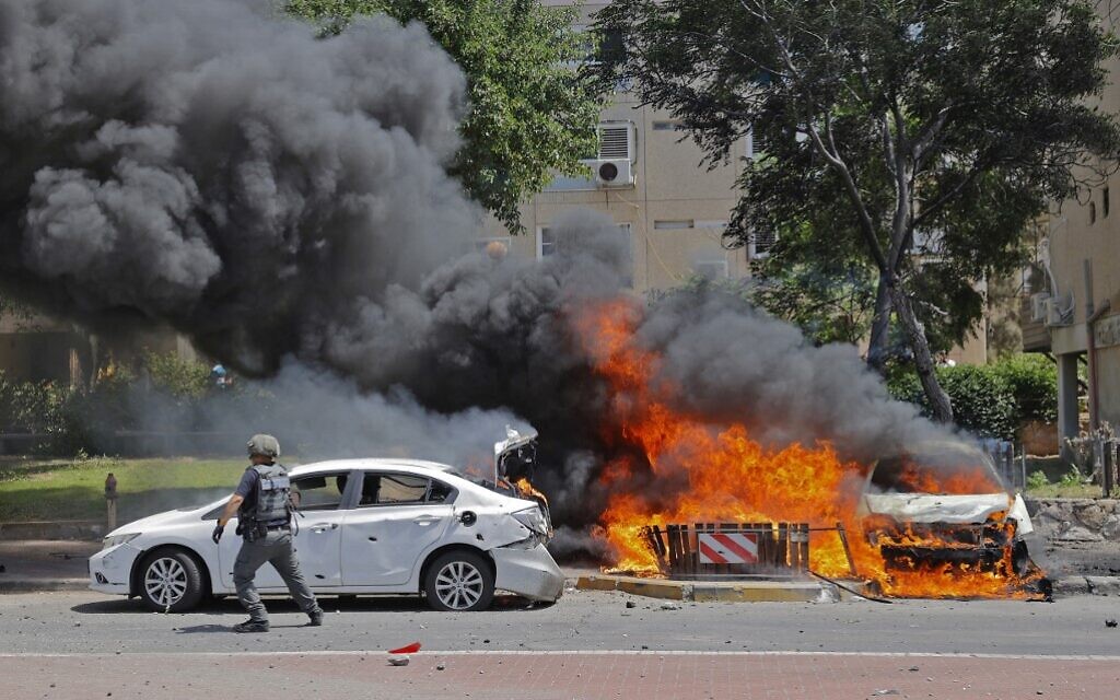 An Israeli soldier runs past a burning vehicle after a rocket launched from the Gaza Strip, controlled by the Palestinian Hamas movement, landed in the southern Israeli city of Ashkelon on May 11, 2021.